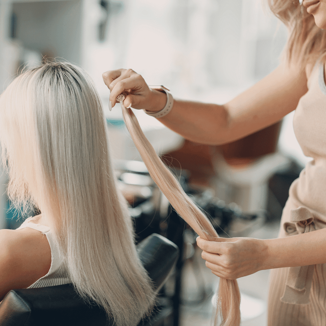 Stylist examining client's long blonde hair at a salon.