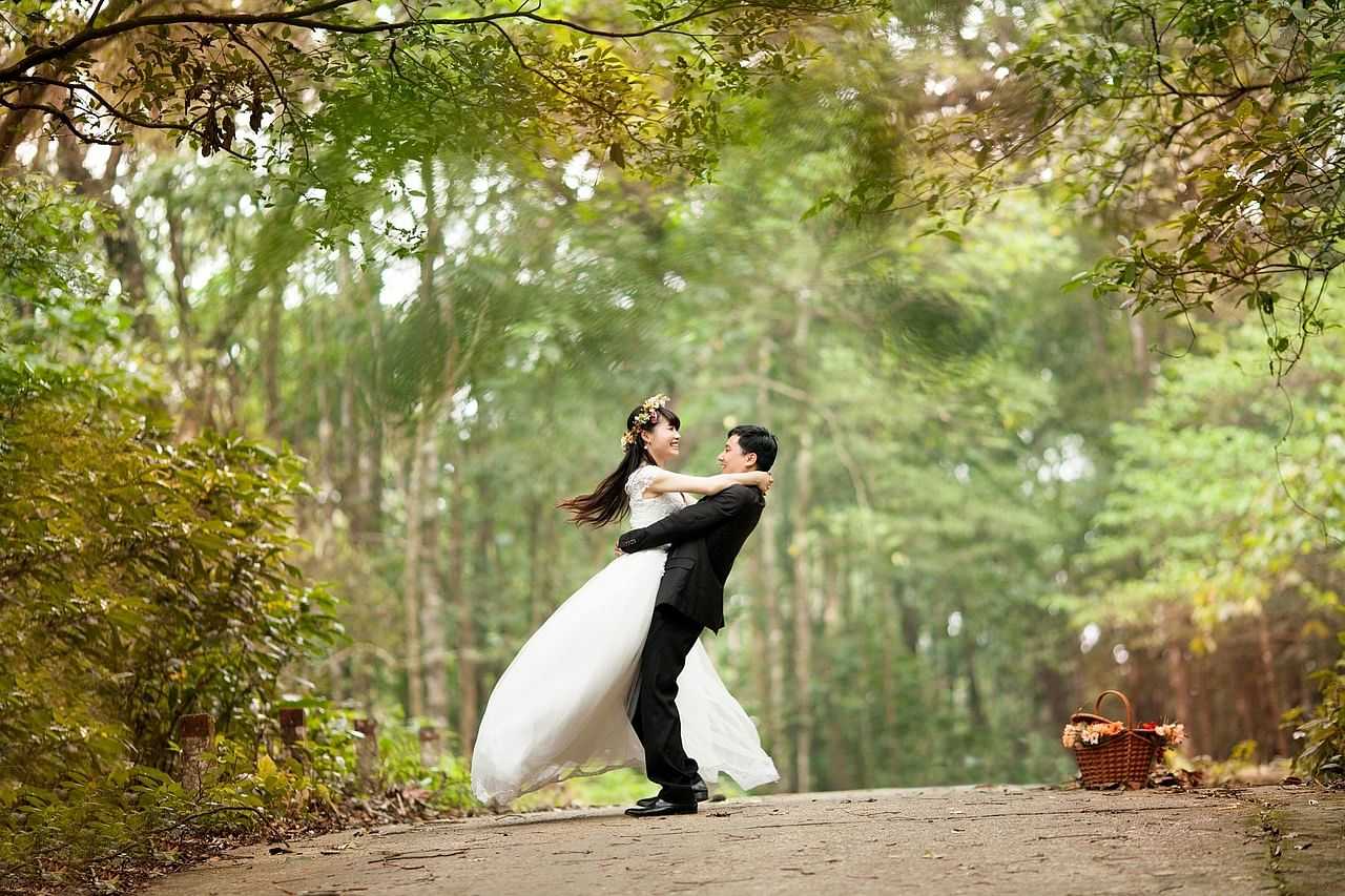 A couple in wedding attire dancing on a forest path.